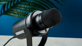 a black microphone with a desktop stand and a black muff is on top of a beige surface with a blue backdrop