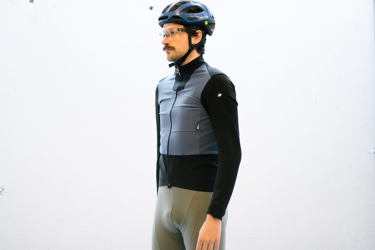 A white man standing in front of a white wall wearing a blue and black winter cycling jacket