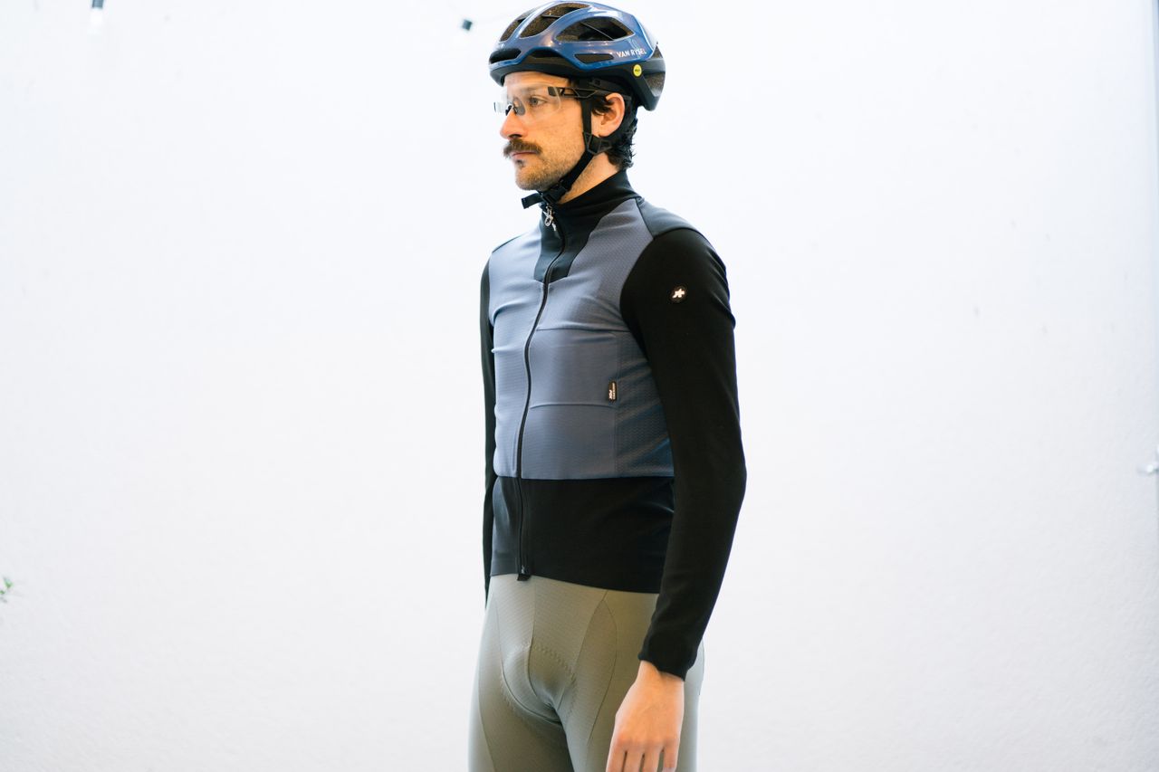 A white man standing in front of a white wall wearing a blue and black winter cycling jacket