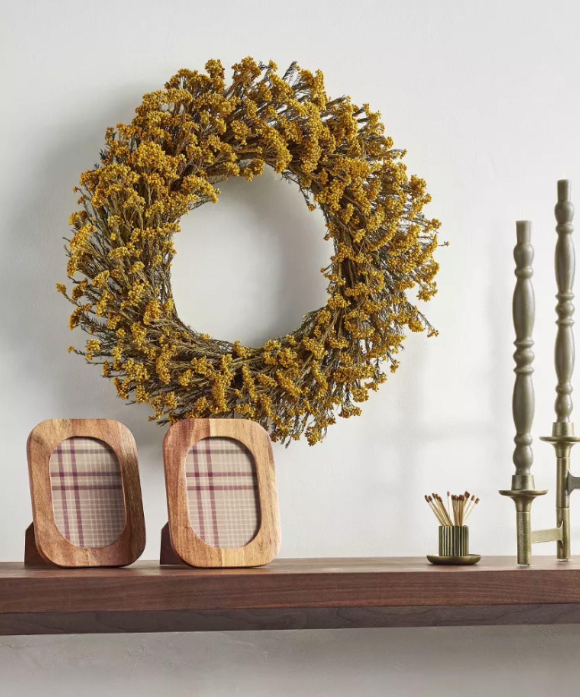 Yellow faux dried flower wreath hung on wall over a shelf with candles and wooden photo frames