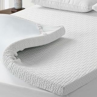 A thick memory foam mattress topper on a bed with one corner curled back
