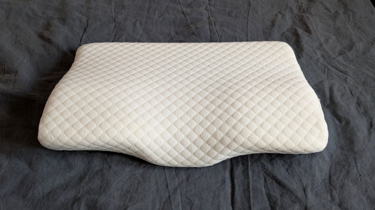 The Kally Sleep Neck Pain Pillow on a grey linen duvet