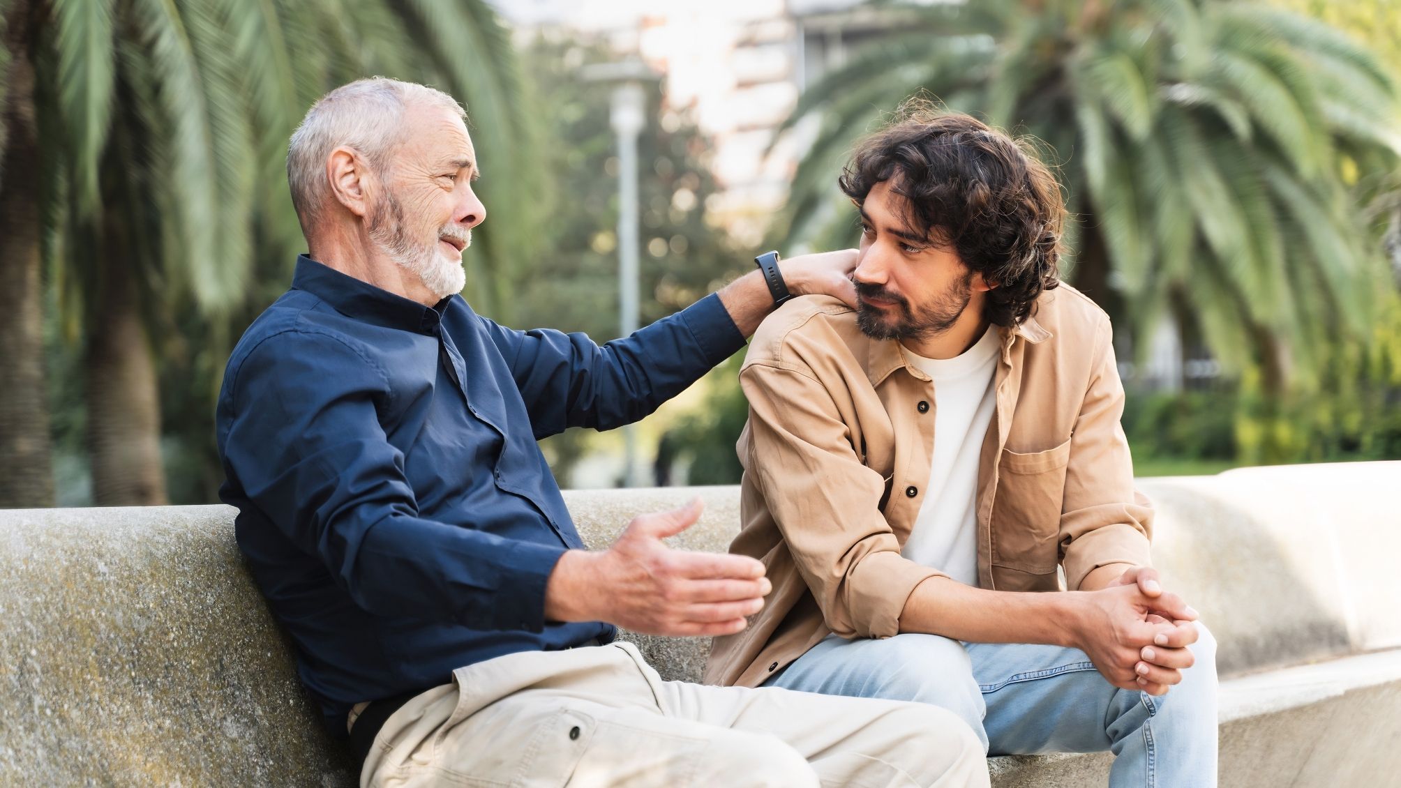 A father and son talking while sitting on a bench in a park. 