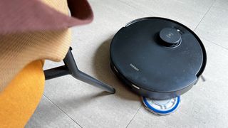 The Ecovacs Deebot T30 Pro Omni robot vacuum mopping near a chair leg with a mop pad extended