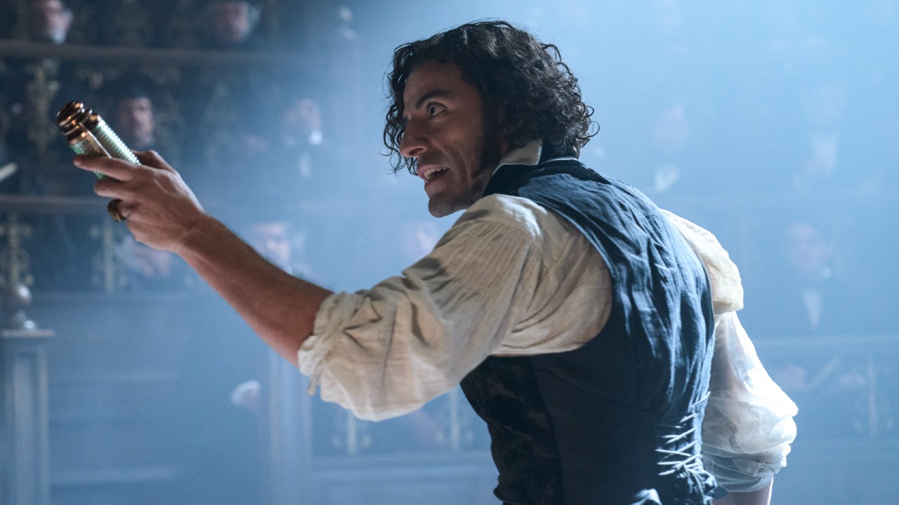 Oscar Isaac as Victor Frankenstein facing a crowd and holding up a bottle in his left hand.