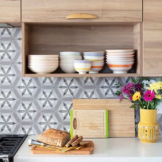 kitchen with hexagon nature patterned tiles open shelves wall cabinets with a half height top hung door chopping boards and flower vase