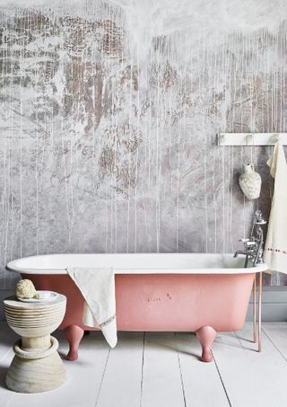 bathroom with textured accent wall, pink painted tub, white painted floor, wooden stool, peg rail