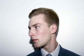 Male modeling looking to the left with smoothed back hair and wearing blue suit