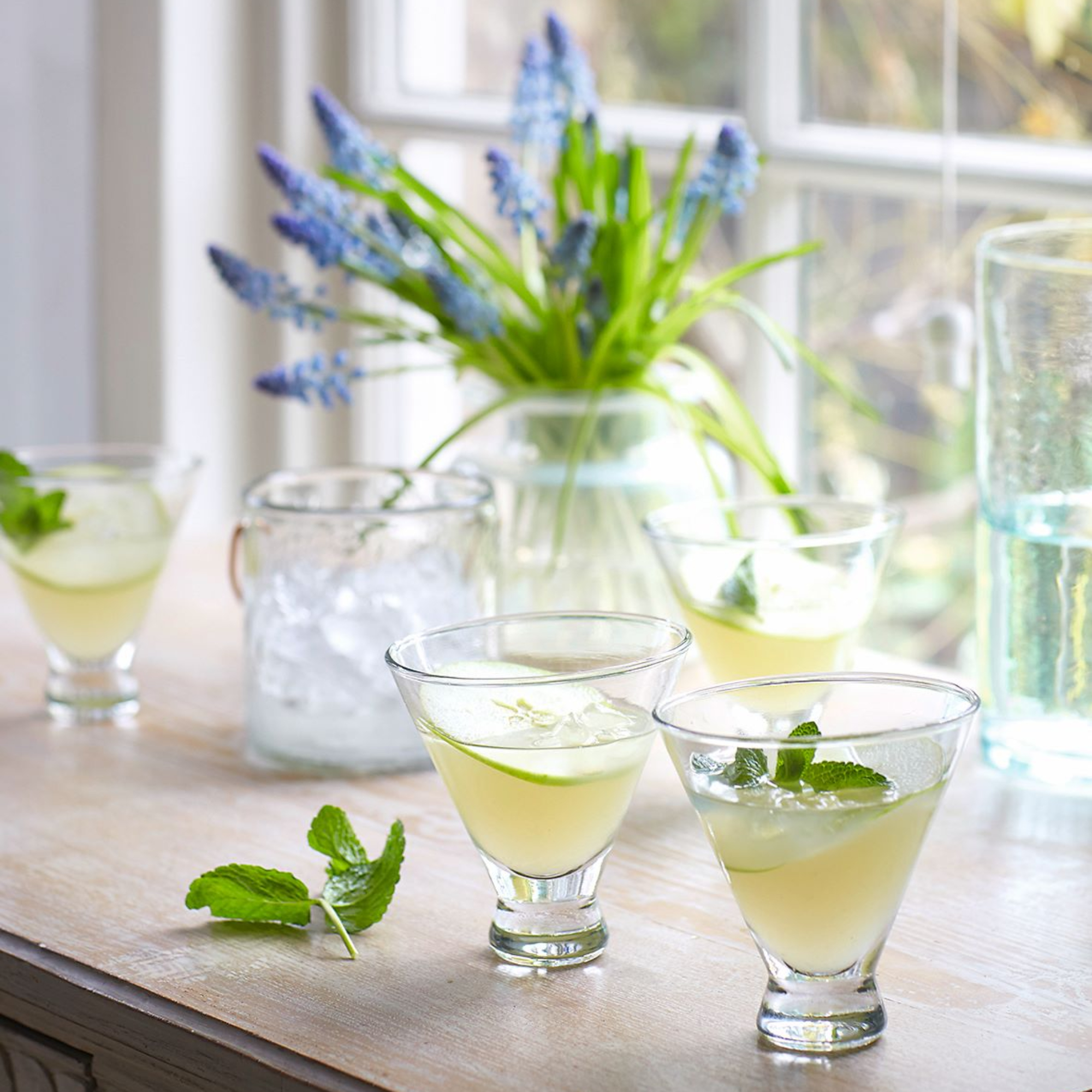 Apple and Elderflower Martini drinks on a wooden table was a glass vase of flowers in front of a window