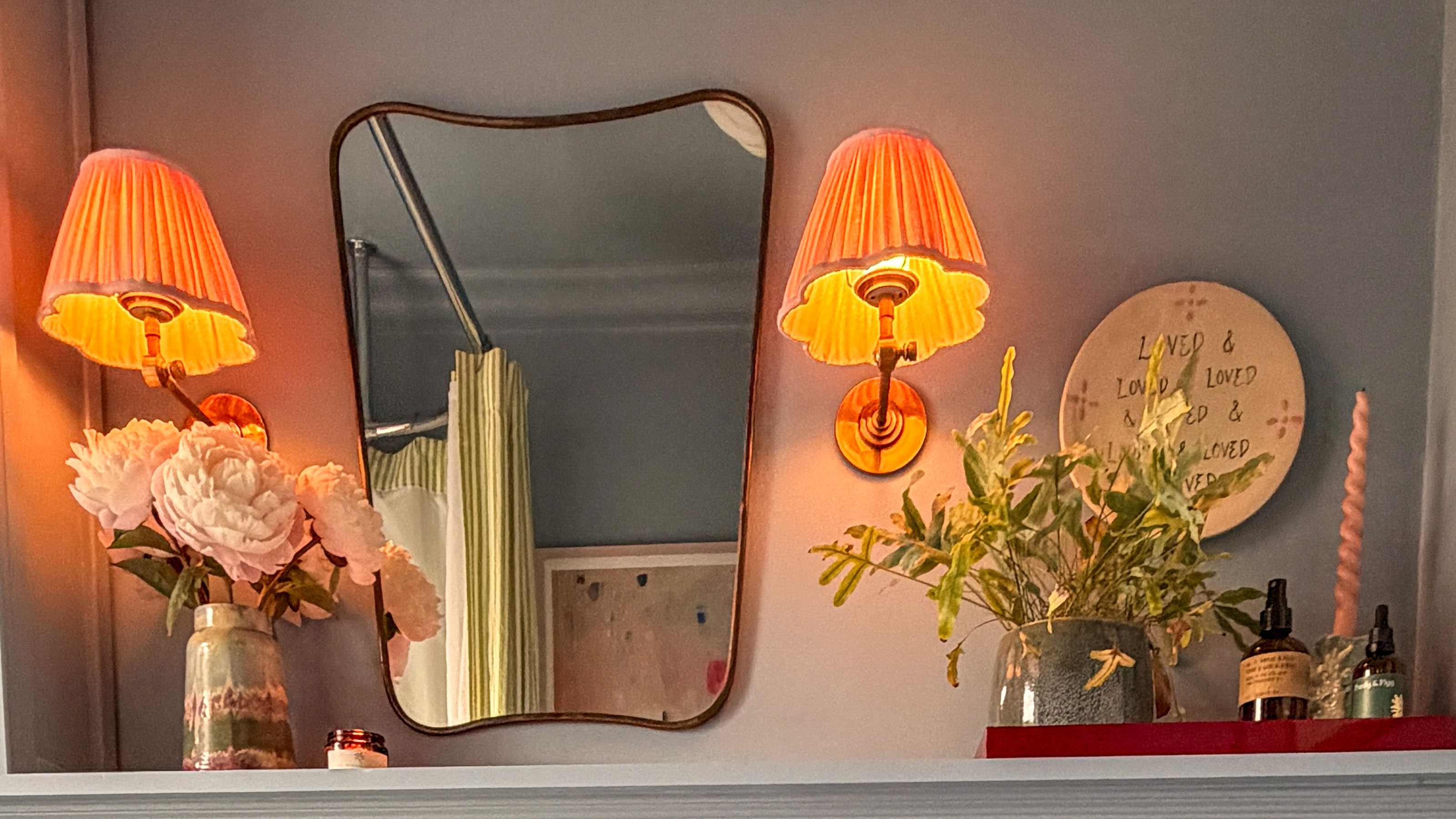 Bathroom shelf with wall mirror, two wall lights and vases of flowers