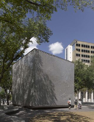 A textured large metal cube on the edge of a public square