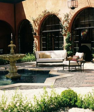 european inspired outdoor space with terracotta arched walls and wrought iron furniture sat by a large outdoor fountain