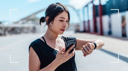 Woman holding smartphone with headphones in by the beach, looking at smartwatch on wrist after learning what is a Fitbit and how to use one