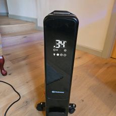 black oil filled radiator showing LED display on wooden floor