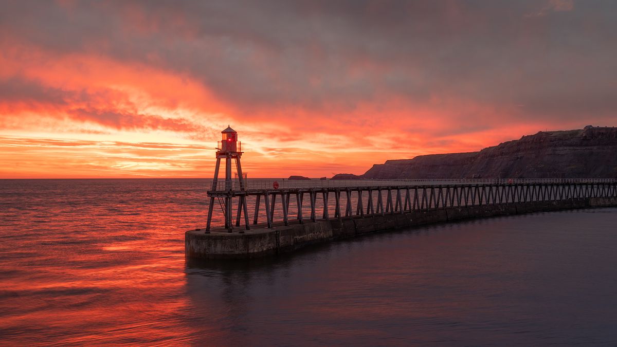 Whitby&#039;s West Pier at sunrise against a fiery orange sky 