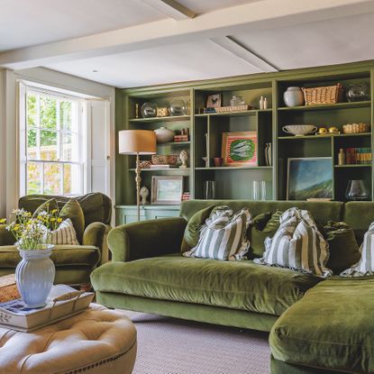 Sitting room with l-shaped green velvet sofa and fitted bookshelves