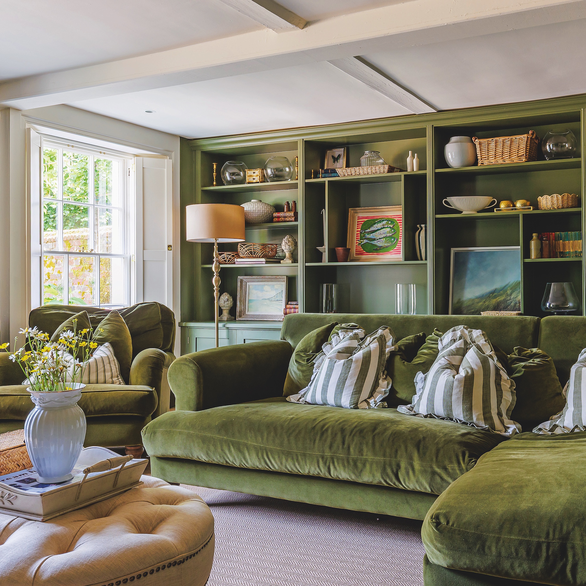 Sitting room with l-shaped green velvet sofa and fitted bookshelves