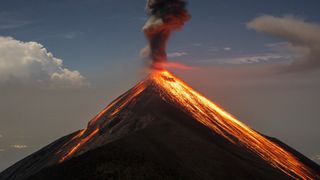 The volcano Fuego (Volcán de Fuego) erupting, spewing red-hot lava and billowing black smoke.