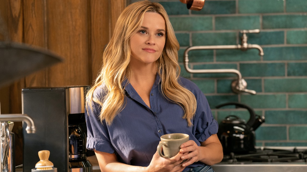 Reese Witherspoon on The Morning Show looking content and holding a coffee mug with both hands. 