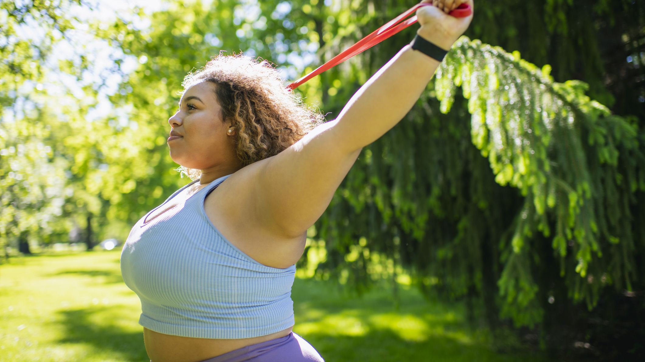 Woman in a park holding a resistance band above her head