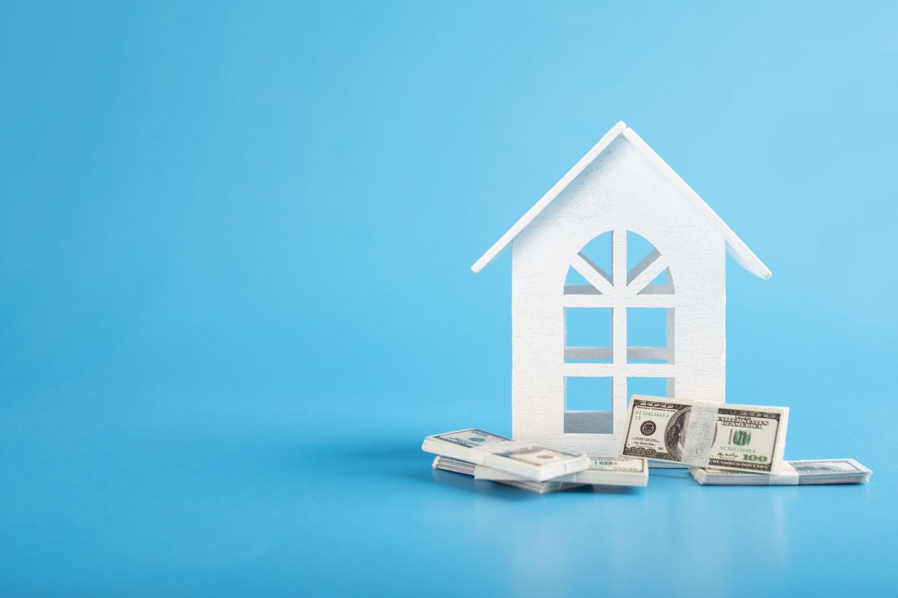 rendering of white home cutout on a stack of money against blue background