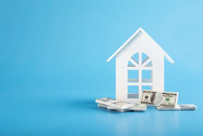 rendering of white home cutout on a stack of money against blue background