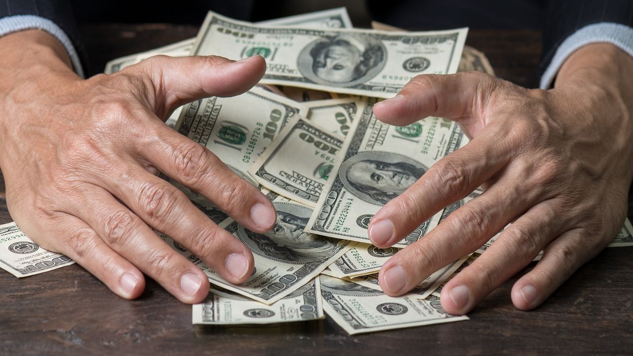 Only a businessman&#039;s hands show as he pulls a pile of cash toward him.