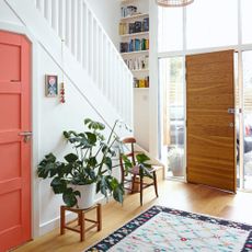 White painted hallway with a wooden front door and wooden floors, and a colourful rug on the floor