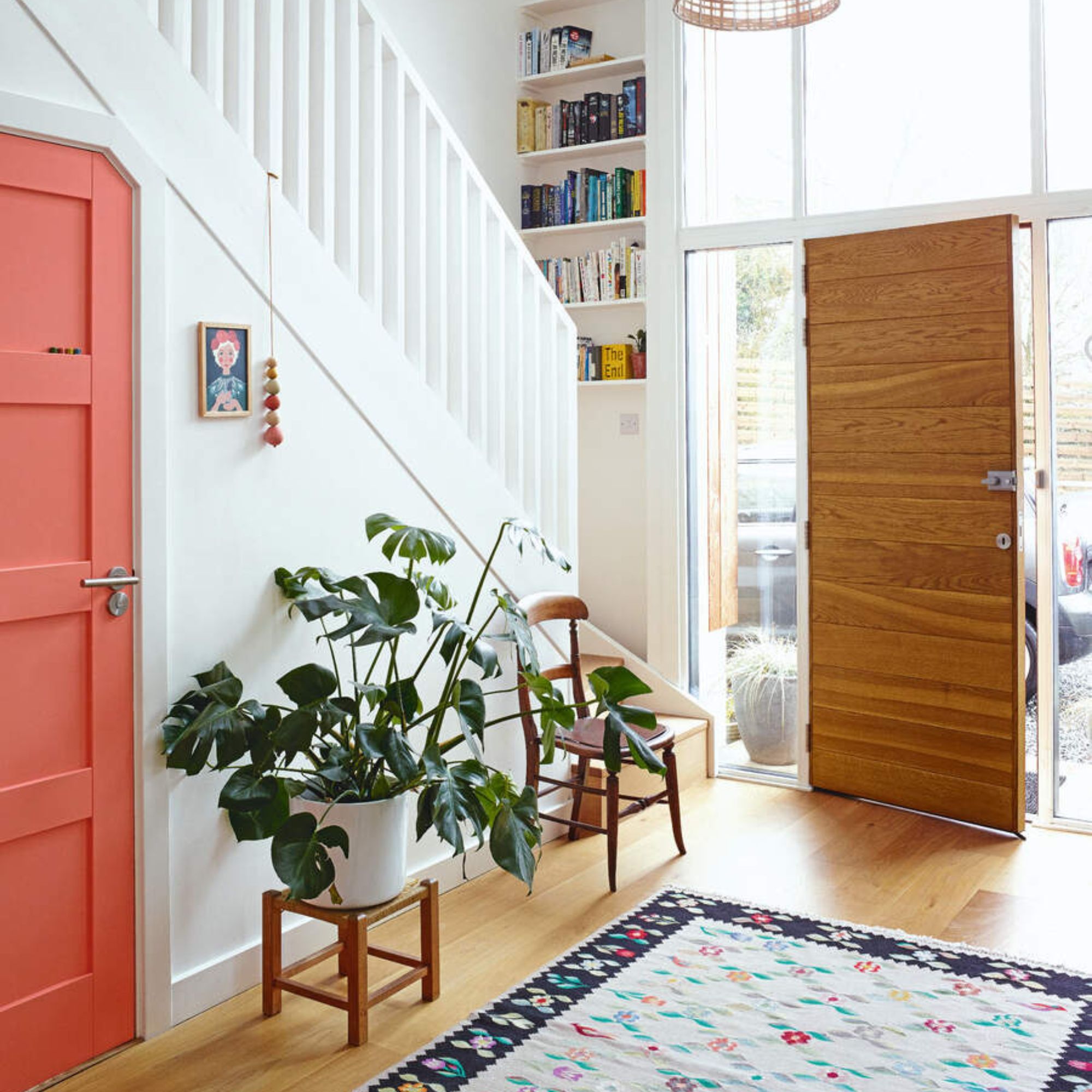 White painted hallway with a wooden front door and wooden floors, and a colourful rug on the floor