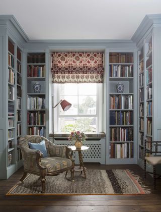 blue bookshelf in reading room with armchair rug and red patterned blinds