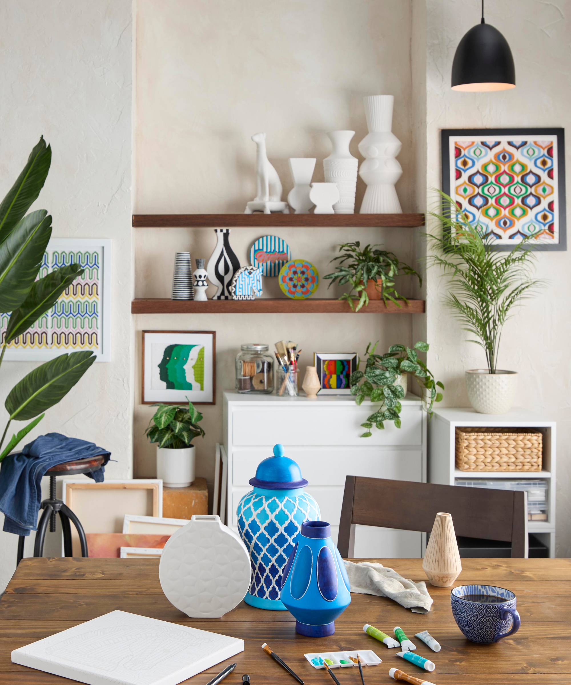 a craft room with vases to paint on a wood table and shelves of pottery in the background