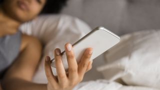 African American woman laying on bed texting on cell phone