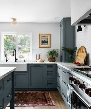 A kitchen with white walls, dusty blue cabinetry and a red vintage rug