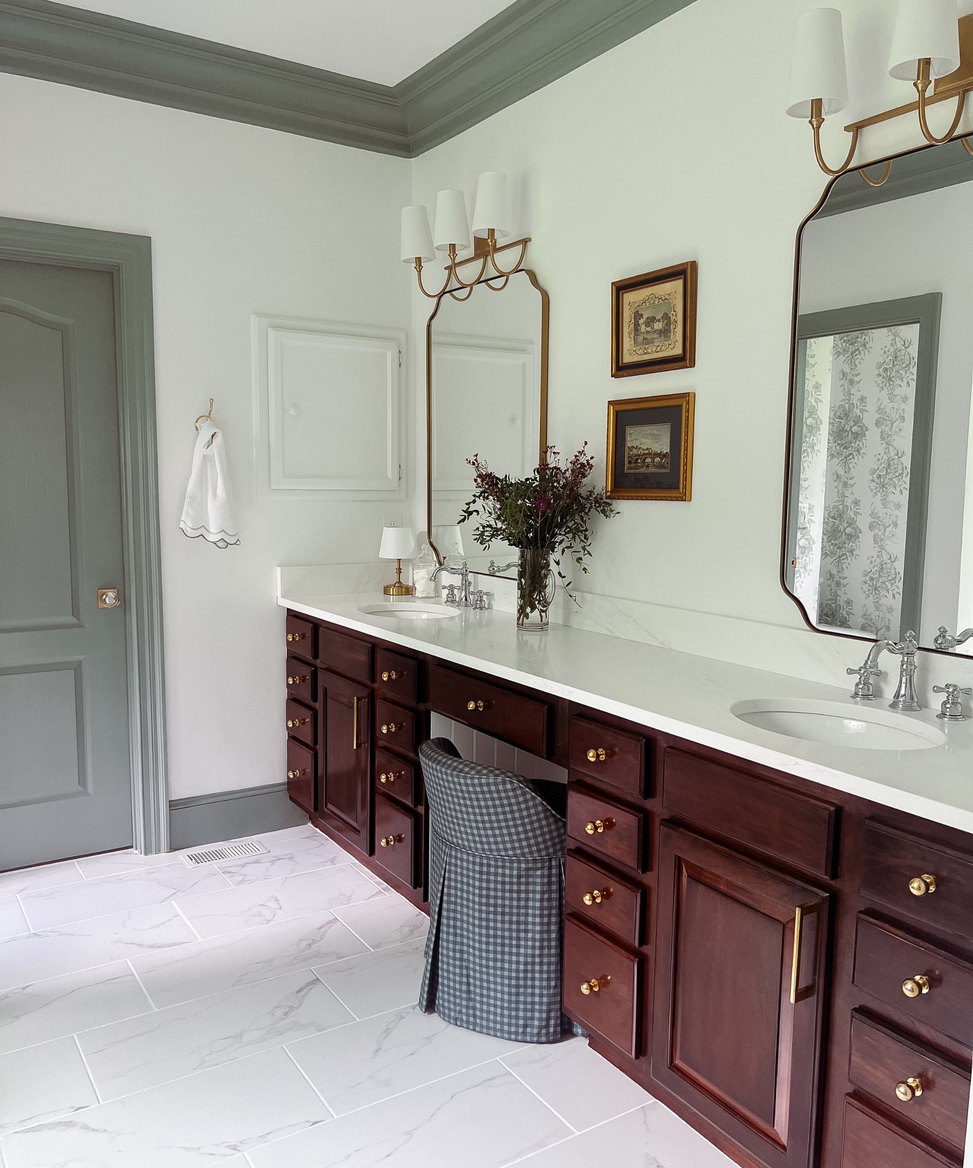 Bathroom with dark mahogany cabinets, double sink, cream walls, gold sconces and large mirrors, vintage prints, and grey trim and painted door frame