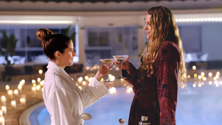Anna Kendrick and Blake Lively in Another Simple Favor. They are wearing bathrobes and standing in front of what appears to be a spa pool surrounded by candles.