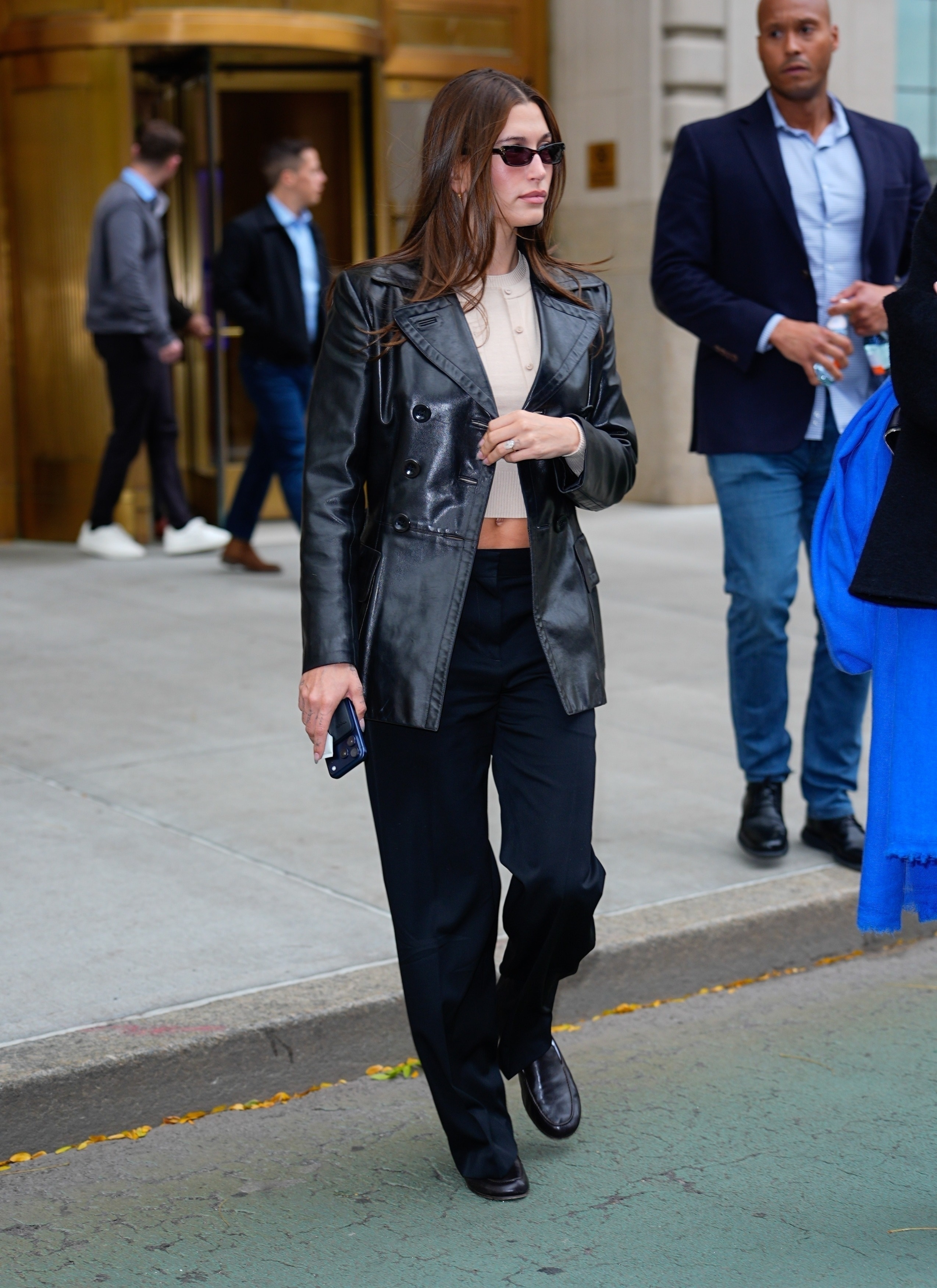 Hailey bieber wears a leather blazer, crop top, black pants, and ablack leather loafers.