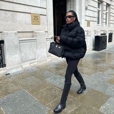 Fashion influencer @nlmarilyn in London wearing an all-black winter outfit with black knee-high riding boots, black leggings, a black puffer jacket, and black accessories.