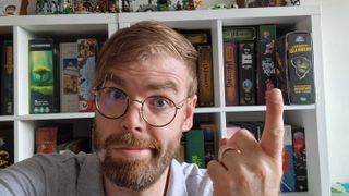 GamesRadar+ Tabletop editor Ben Abbott pointing at collection of board games on a shelf