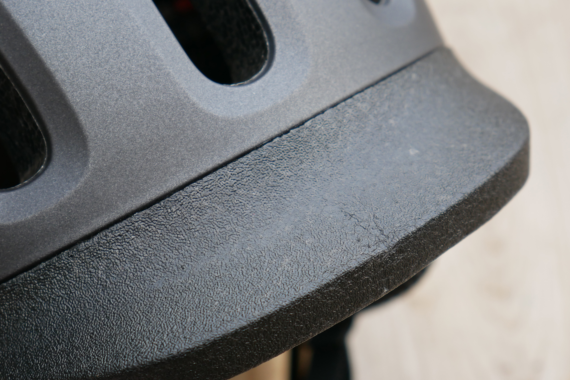 small dent made in the peak of Woom Ready Kids Bike Helmet in black against a backdrop of a wooden deck