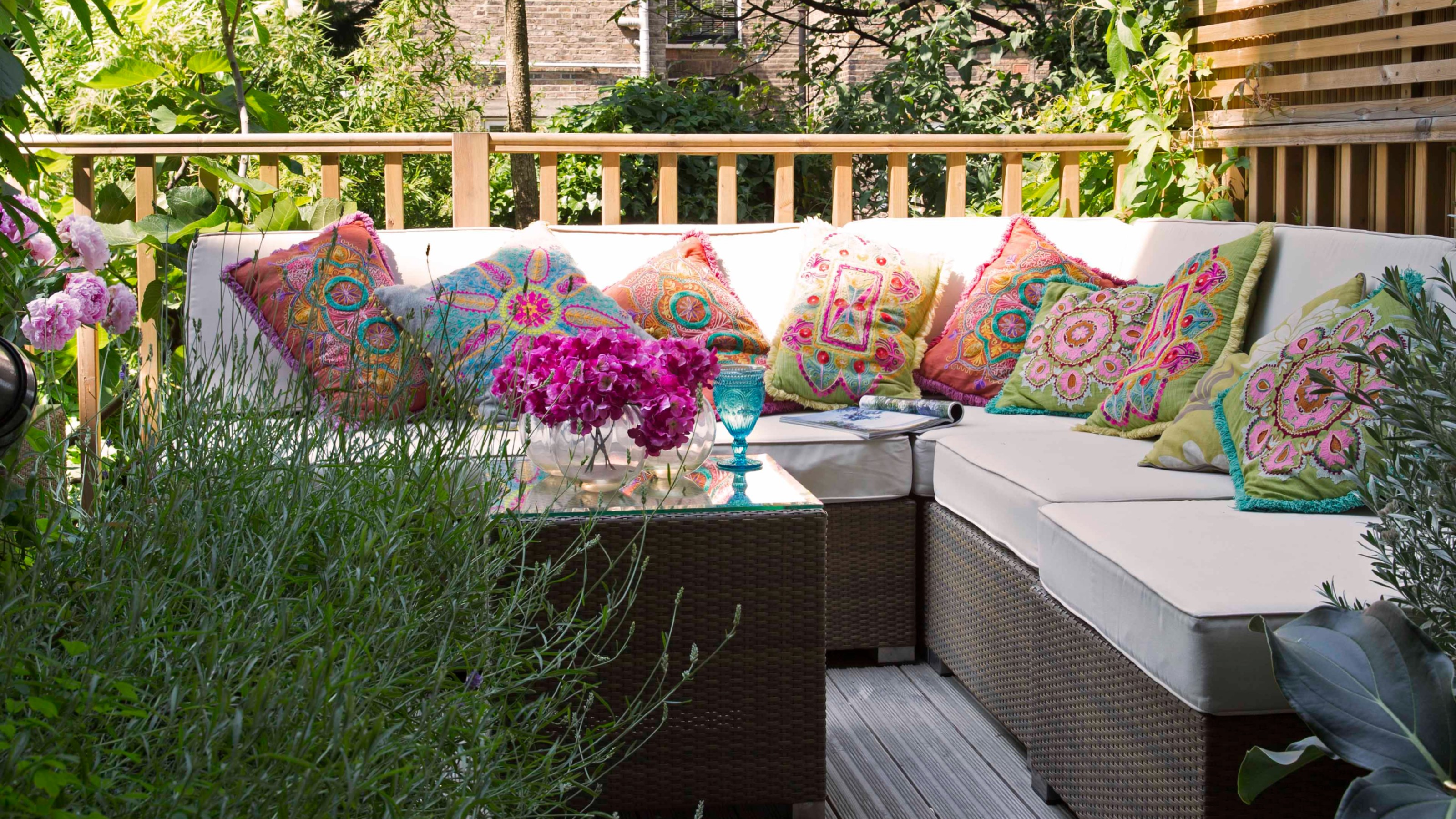 A balcony with a corner modular sofa in a rattan effect decorated with colourful patterned outdoor cushions