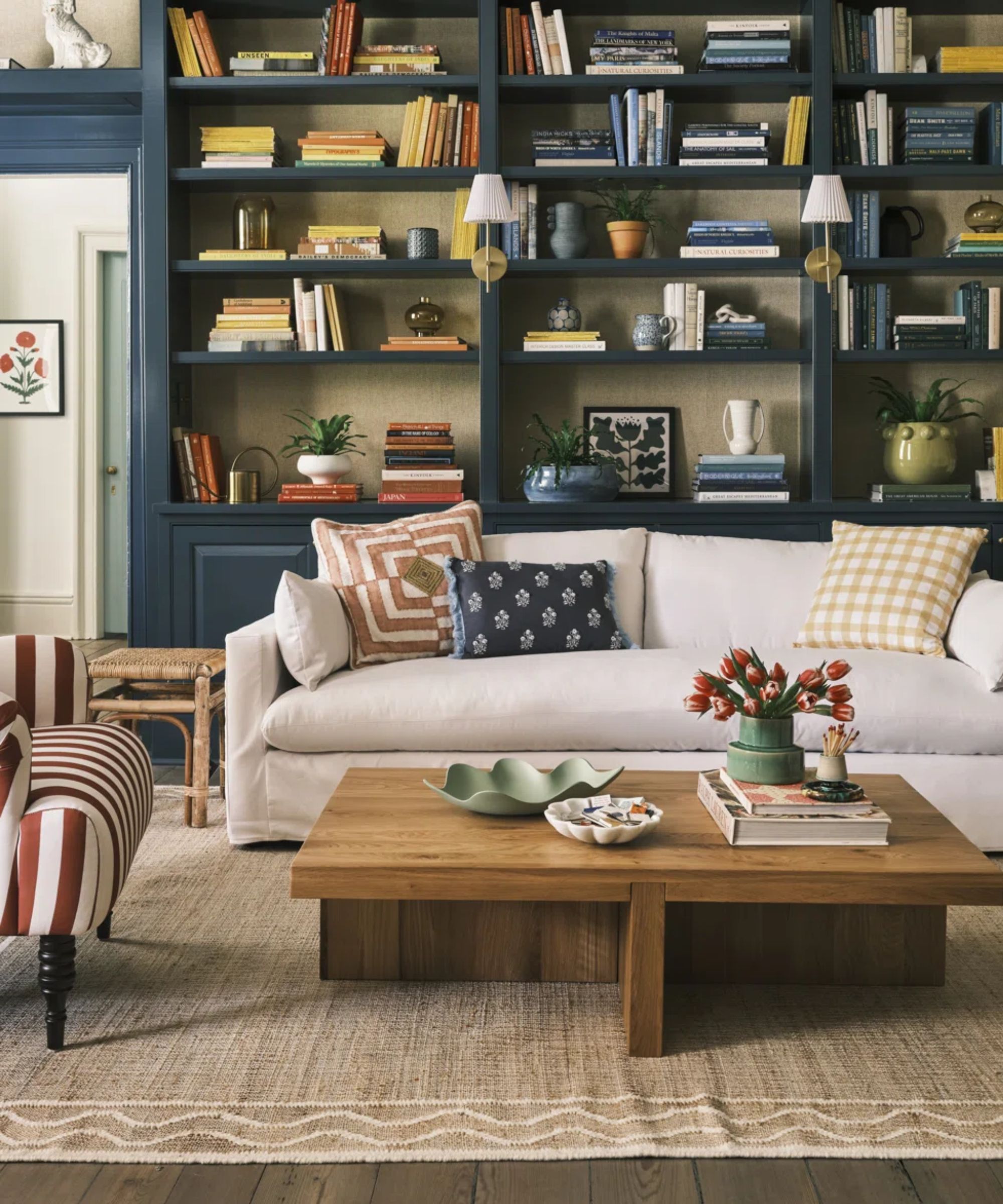 navy blue living room with bookshelves, a neutral couch with floral and plaid cushions, red and white striped armchair, a wooden coffee table and a jute rug with wave details