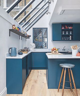 A kitchen extension with a sloping glass roof, blue cabinets and an island with an industrial style bar stool