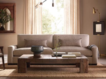 A linen sofa in grey with two throw pillows in natural material in front of a window