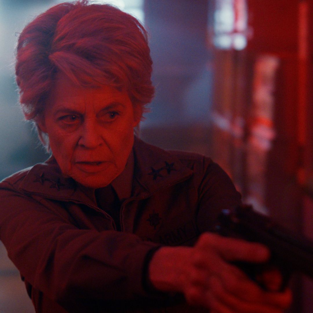 linda hamilton as dr. kay pointing a gun walking down a dimly red lit hallway in stranger things season 5