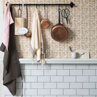 copper pan hanging on storage rail in kitchen with white and gold wallpapered wall