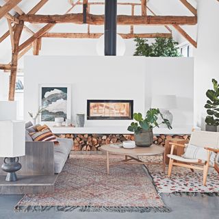 living area with white wall and wooden beam and grey sofa and wooden stacks