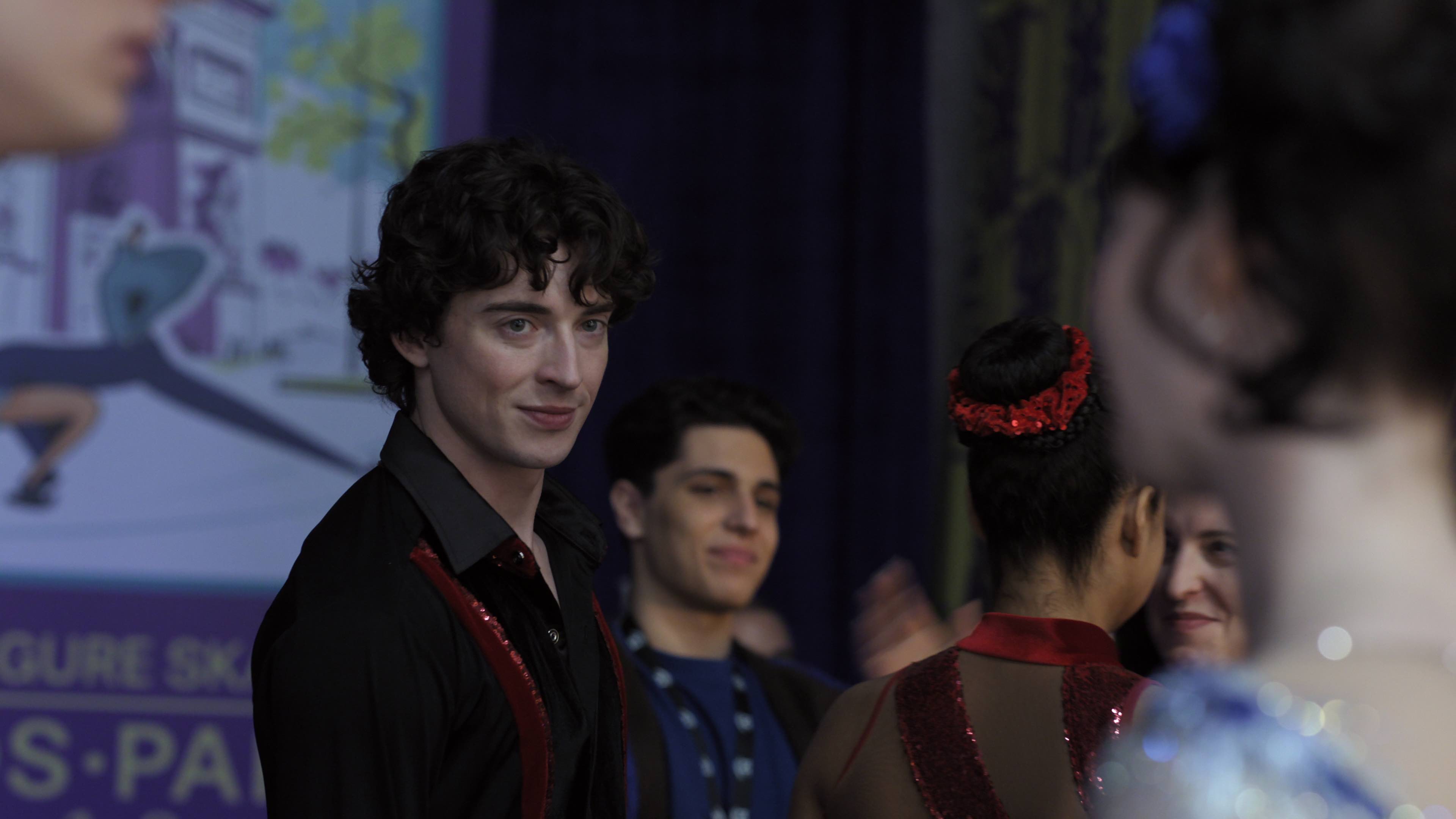 Olly Atkins as Freddie O'Connell wearing a black and red figure skating uniform smirking at a female skater at a competition in a still fromFinding Her Edge: Season 1