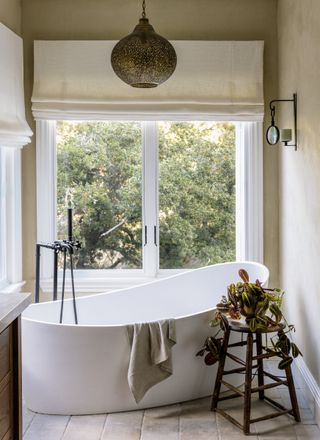 Neutral bathroom with a large window and a curved freestanding bath with large brass pendant lamp