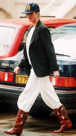 Princess Diana wearing an unusual combination of white trousers, boots, a blazer jacket and a baseball cap after taking her sons to school at Wetherby, 25th April 1989.