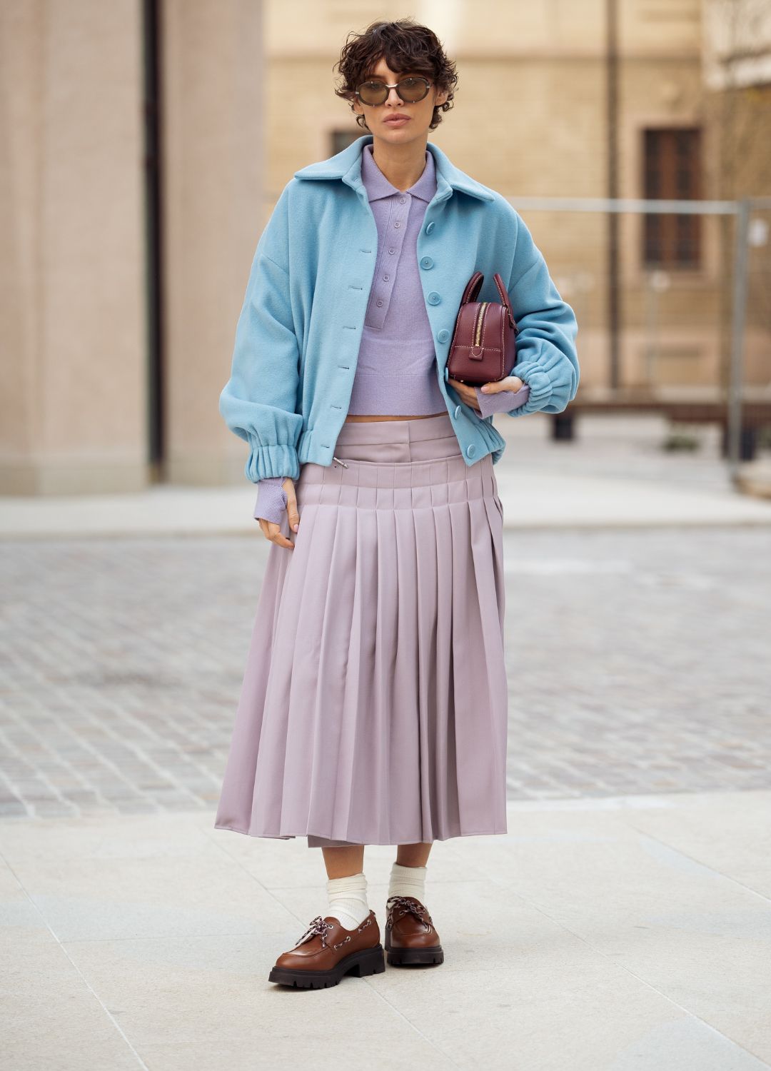 Irina Kro Eicke wears lavender midi skirt with attachable pleated part, matching top with buttons, blue jacket and brown mini bag outside the Bally fashion show during the Milan Fashion Week Womenswear Fall/Winter 2025/2026 on March 01, 2025 in Milan, Italy.